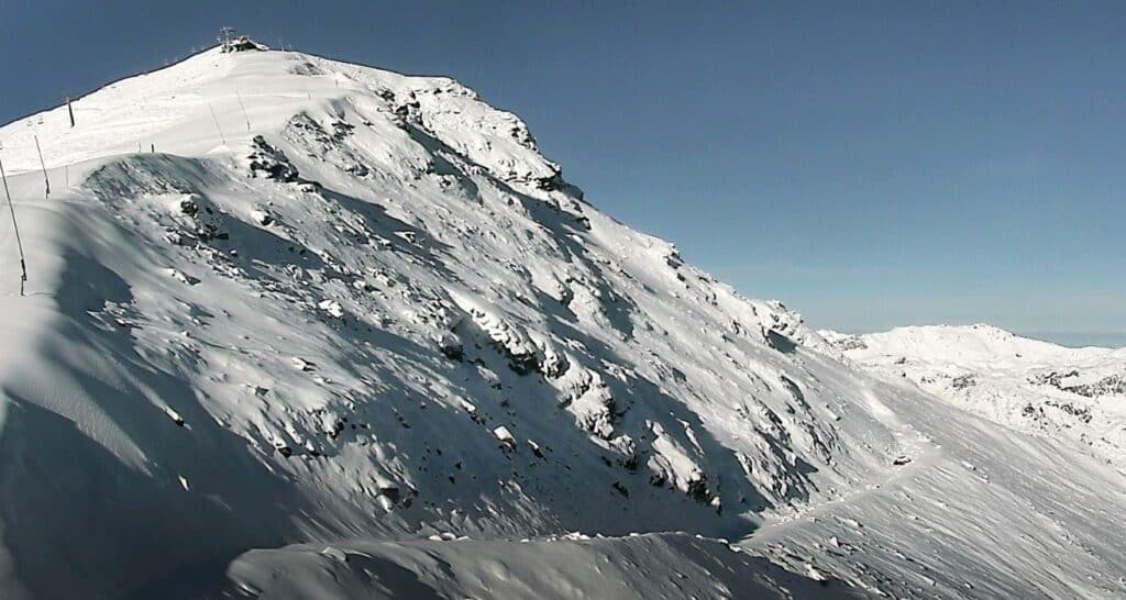 Vue panoramique d'un sommet enneigé sous un ciel dégagé, avec des pentes couvertes de neige.