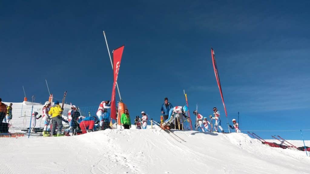 Équipes de skieuses se préparant pour un slalom géant sur une piste enneigée à Zinal sous un ciel bleu.