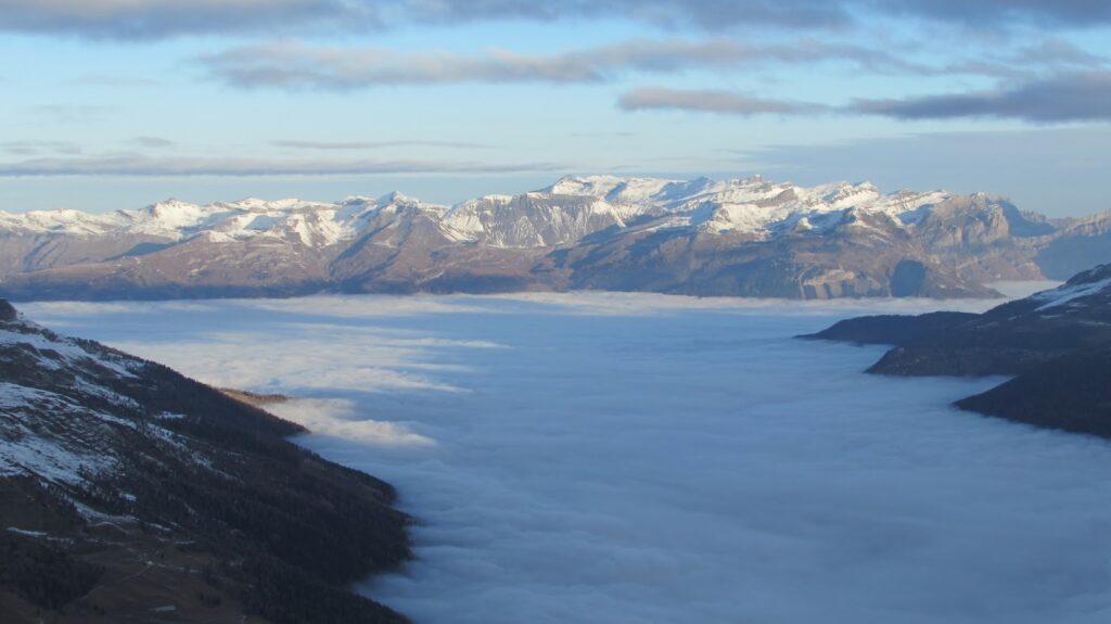 Vue panoramique sur les montagnes enneigées surplombant une mer de brouillard à 1900 mètres d'altitude.