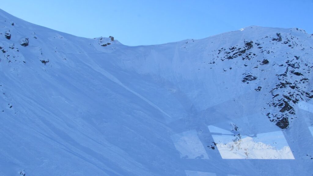 Vue des rochers sous l'arête des 'Valentines' à Durand, avec une montagne enneigée sous un ciel bleu.