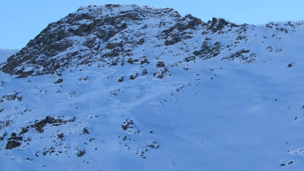 Vue d'une montagne enneigée avec des rochers et des plaques de neige, montrant des traces d'avalanches sur le flanc.