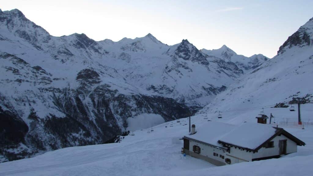 Vue panoramique des montagnes enneigées avec un chalet au premier plan, photographiée tôt le matin dans un domaine skiable.