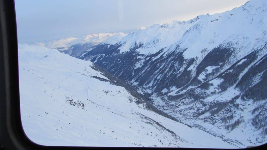 Vue aérienne du vallon de Zinal depuis un hélicoptère, montrant des paysages enneigés avec des montagnes en arrière-plan.