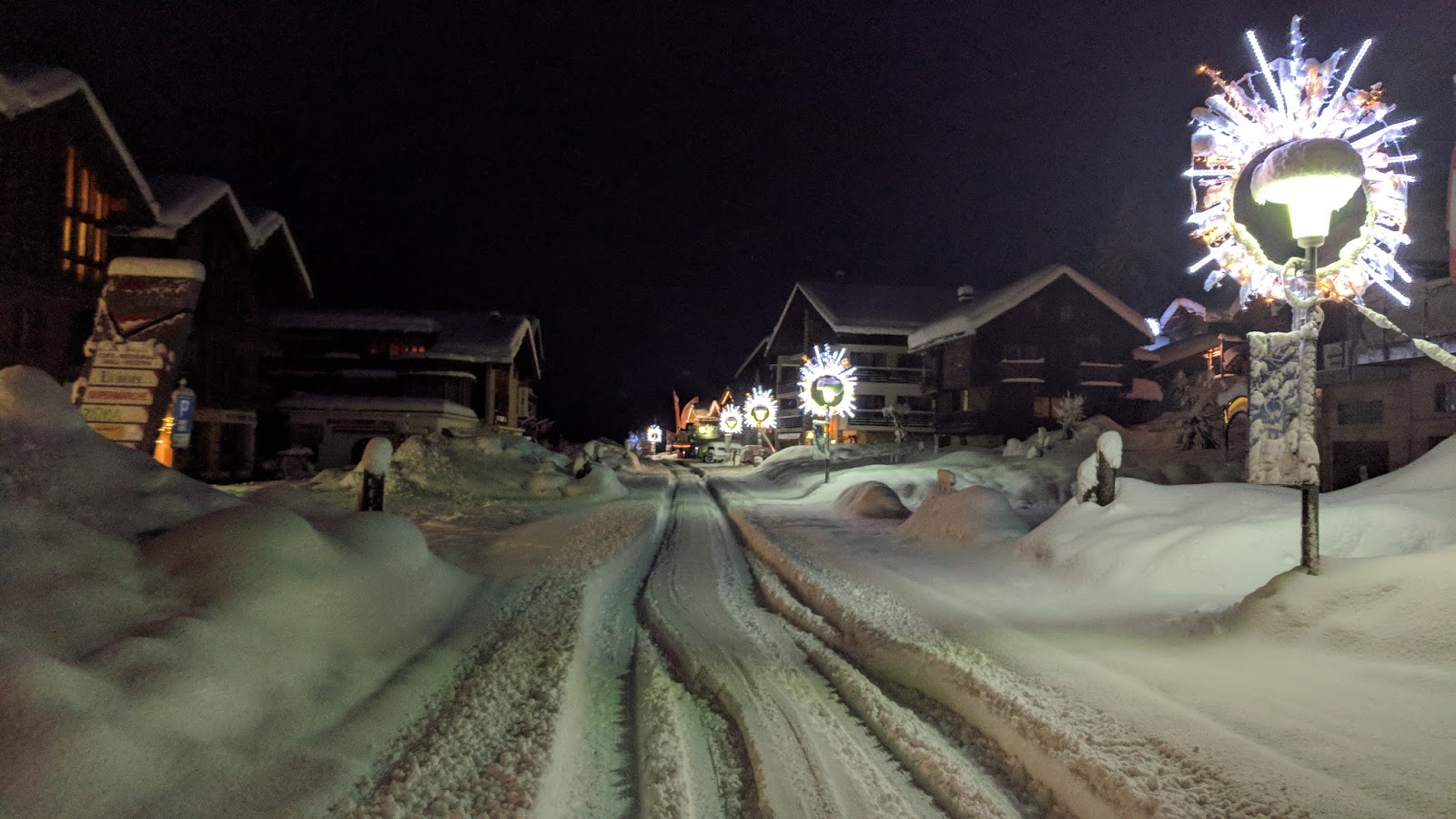 Village alpin enneigé la nuit avec chalets et décorations festives.