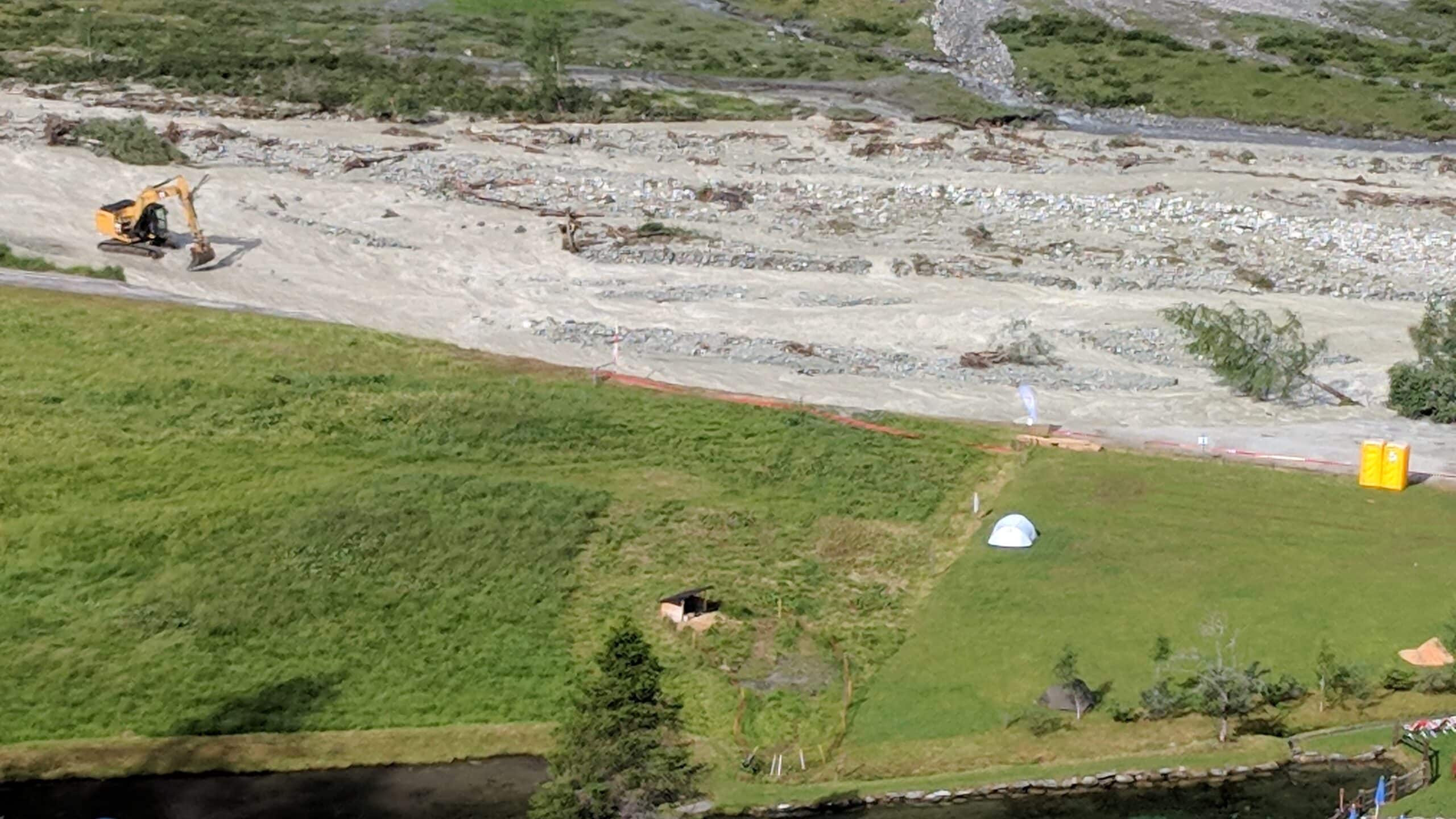 Pelle mécanique dans une rivière boueuse près d'un campement.