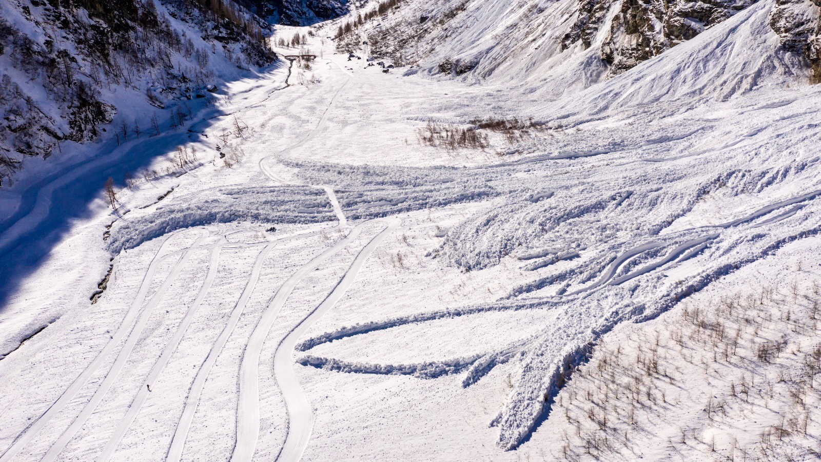 Vaste vallée montagneuse enneigée avec débris d'avalanche et pistes.