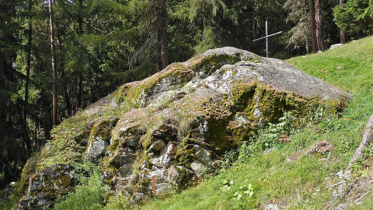 Grosse roche couverte de mousse, forêt et croix en bois.