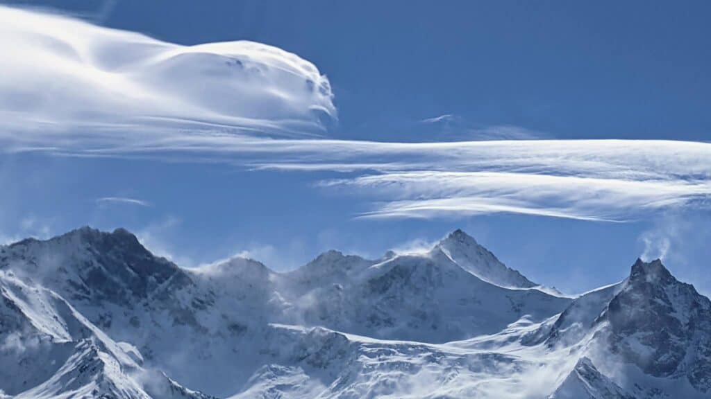 Vue des sommets montagneux sous un ciel bleu avec des nuages en forme de vagues.