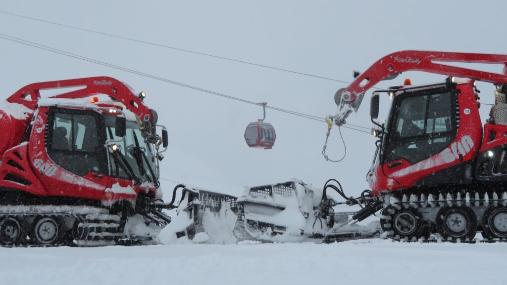 Deux dameuses rouges PistenBully et une télécabine dans la neige.