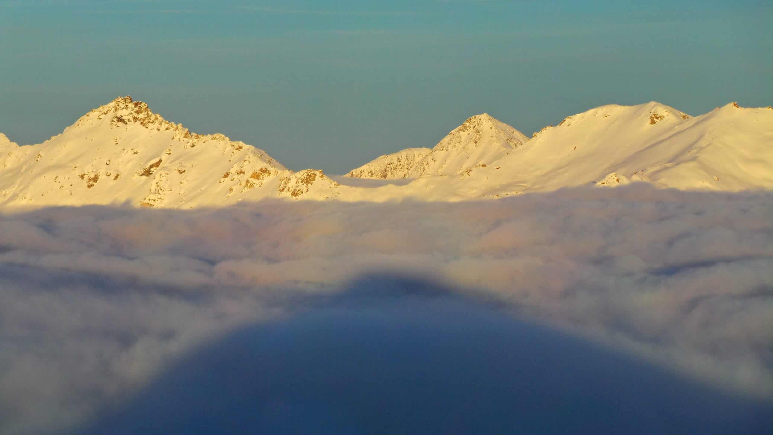 Lever de soleil sur montagnes enneigées au-dessus d'une mer de nuages.