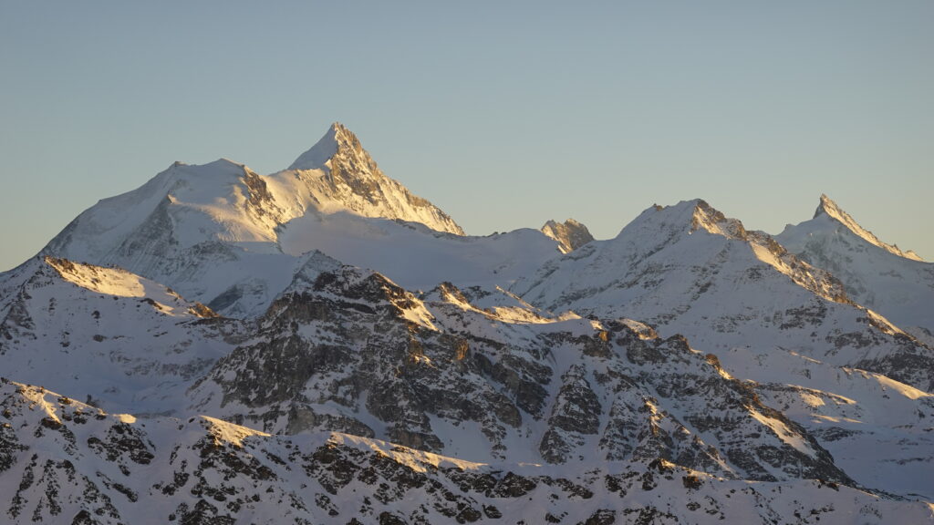 Vue des montagnes enneigées au lever du soleil, mettant en valeur des sommets majestueux.