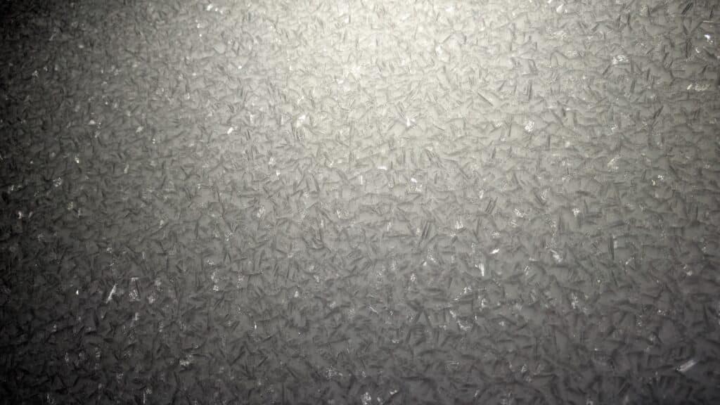 Texture de glace et givre sur une surface plane, reflétant la lumière.