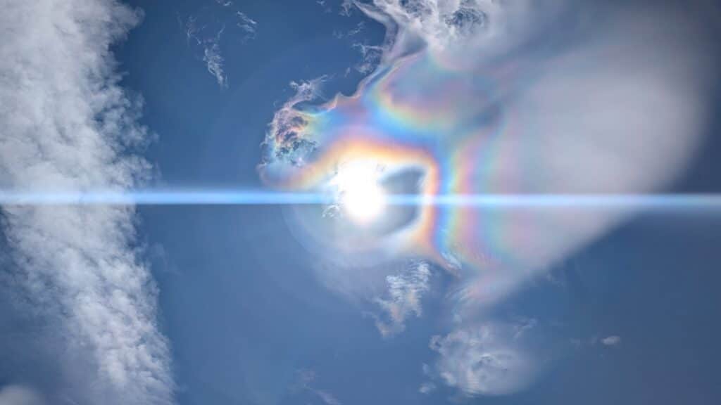 Un spectacle de lumière éclatante dans le ciel, avec des nuages en arrière-plan et un effet d'arc-en-ciel autour du soleil.
