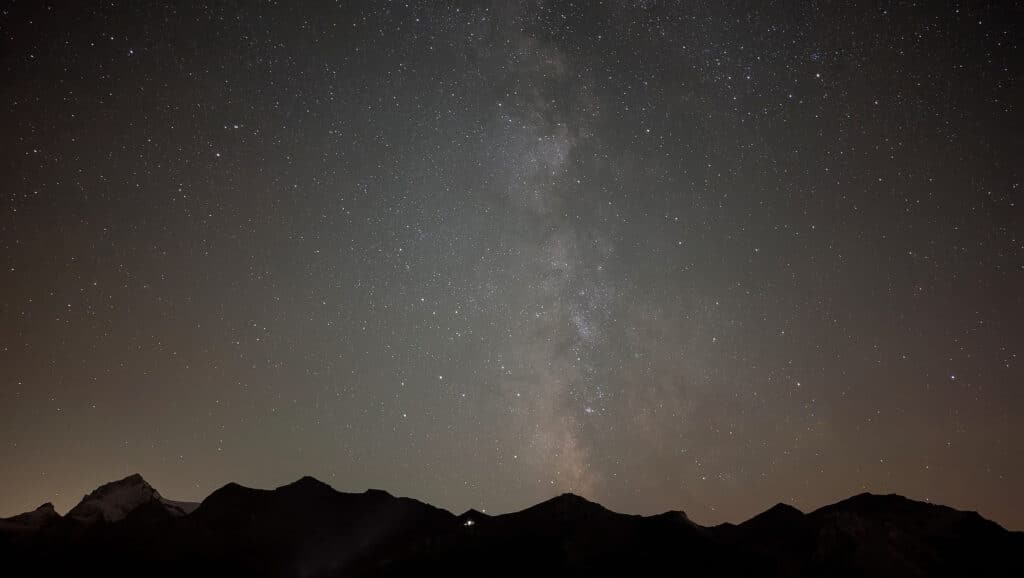 Ciel étoilé avec la Voie lactée surmontant des montagnes sombres, créant une atmosphère nocturne paisible.