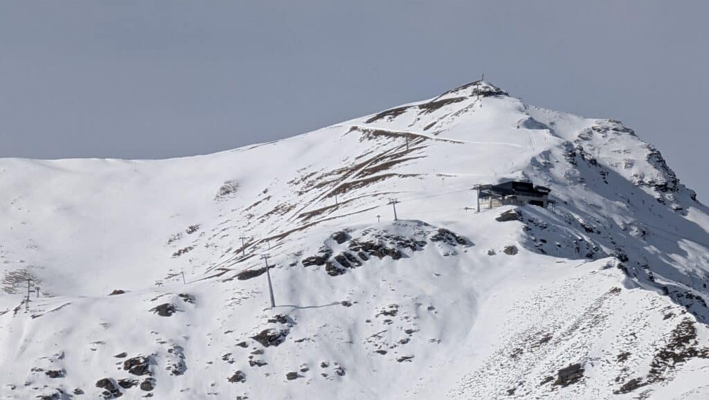 Vue d'un sommet montagneux recouvert de neige avec une station de ski visible sur le flanc.