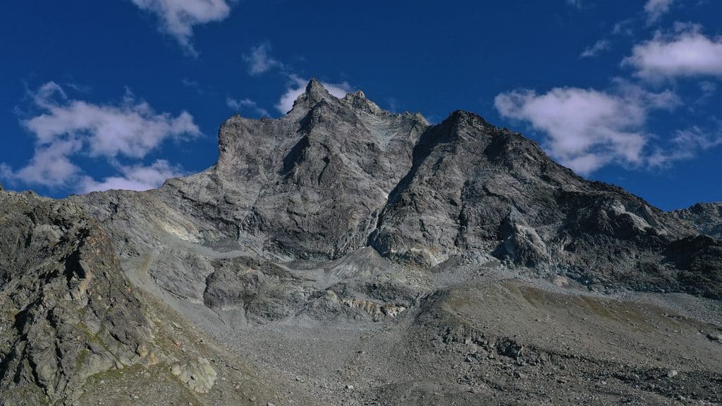 Haute montagne rocheuse sous ciel bleu avec quelques nuages.