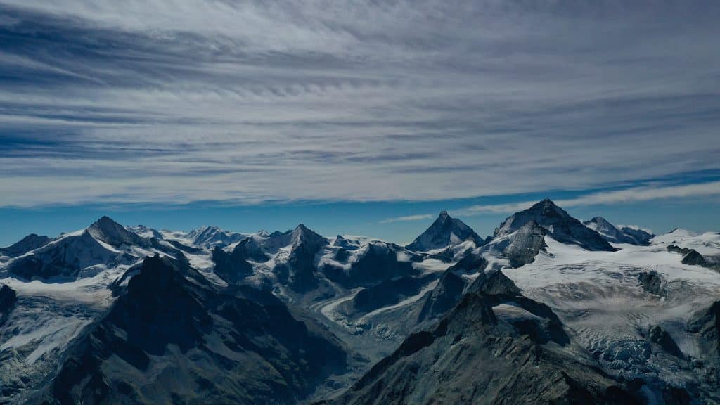 Chaîne de montagnes enneigées avec glaciers sous un ciel nuageux.