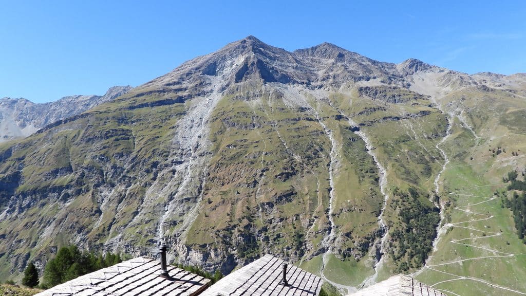 Montagnes alpines, toits en bois, sentier de randonnée sinueux.
