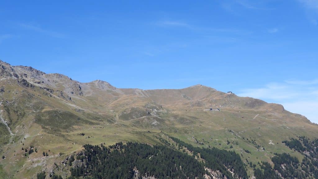 Paysage montagneux alpin avec ciel bleu et remontées mécaniques.
