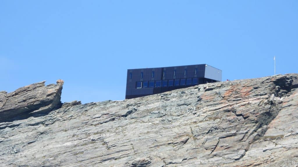 Refuge moderne sur crête rocheuse sous ciel bleu.