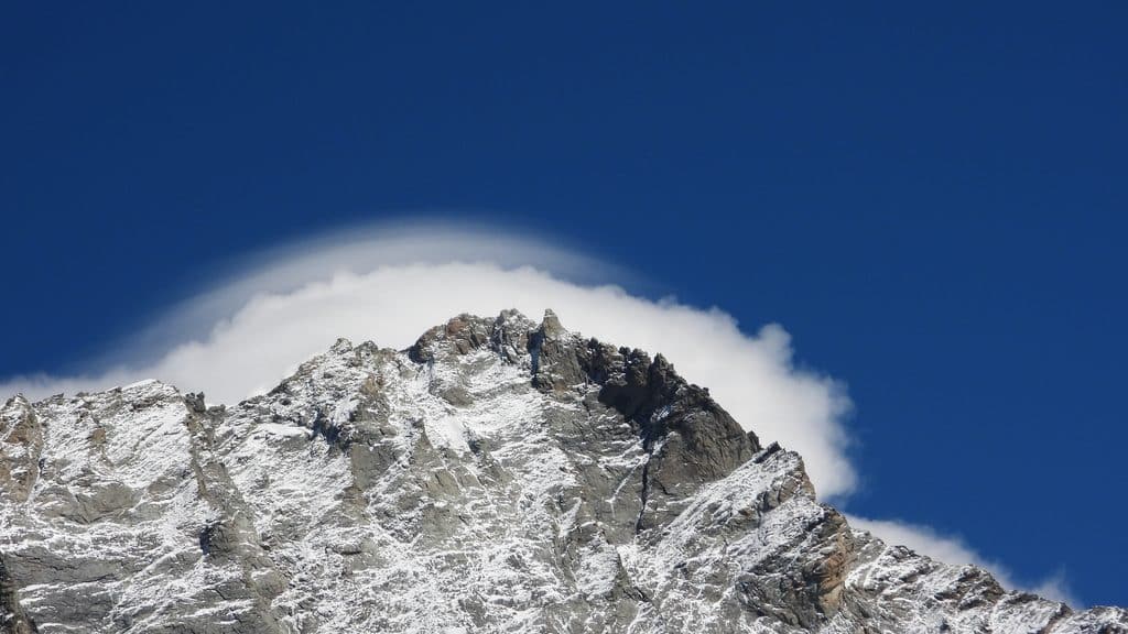 Sommet montagneux enneigé sous ciel bleu et nuage lenticulaire.