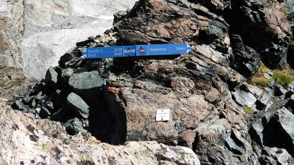 Panneau de randonnée bleu sur rocher, glacier en arrière-plan.