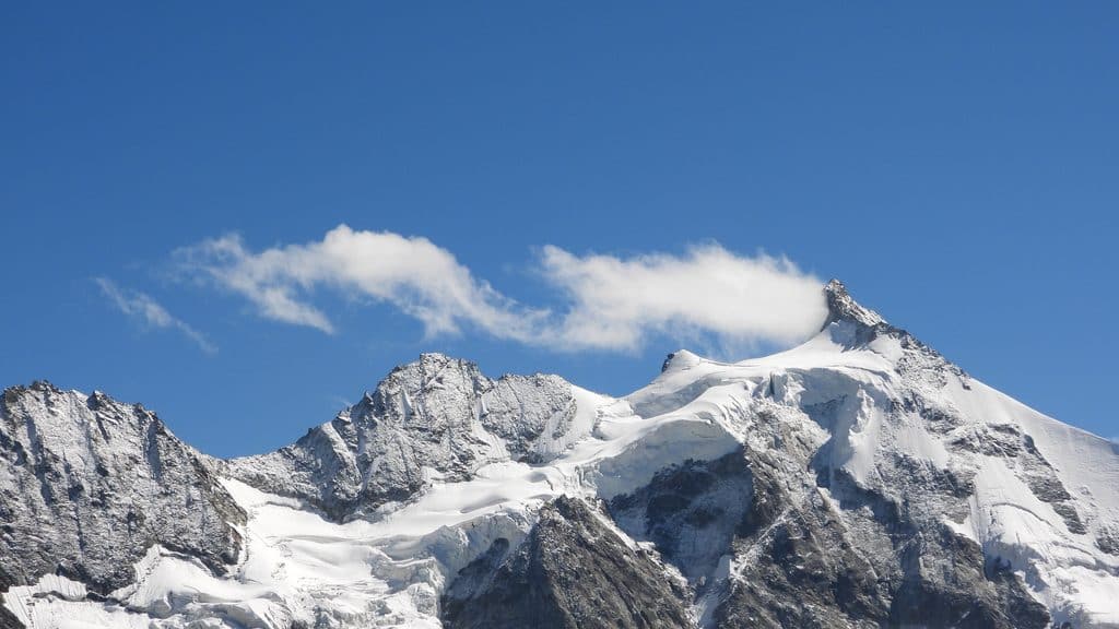 Montagnes enneigées, ciel bleu, nuages fins, paysage alpin majestueux.