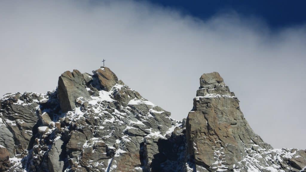 Croix sur un sommet rocheux enneigé sous un ciel nuageux.