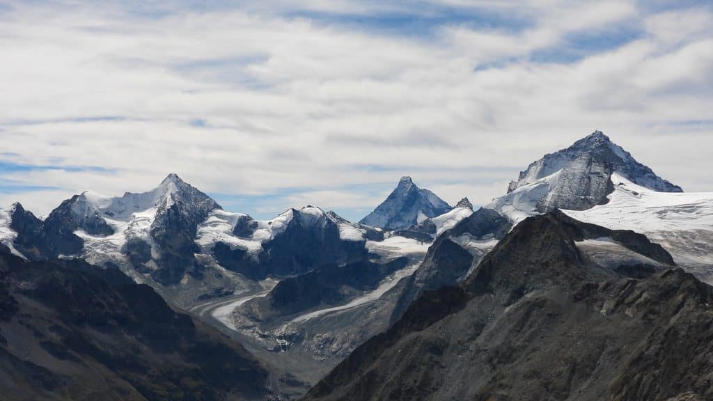 Sommets alpins enneigés, glaciers et ciel nuageux impressionnant.