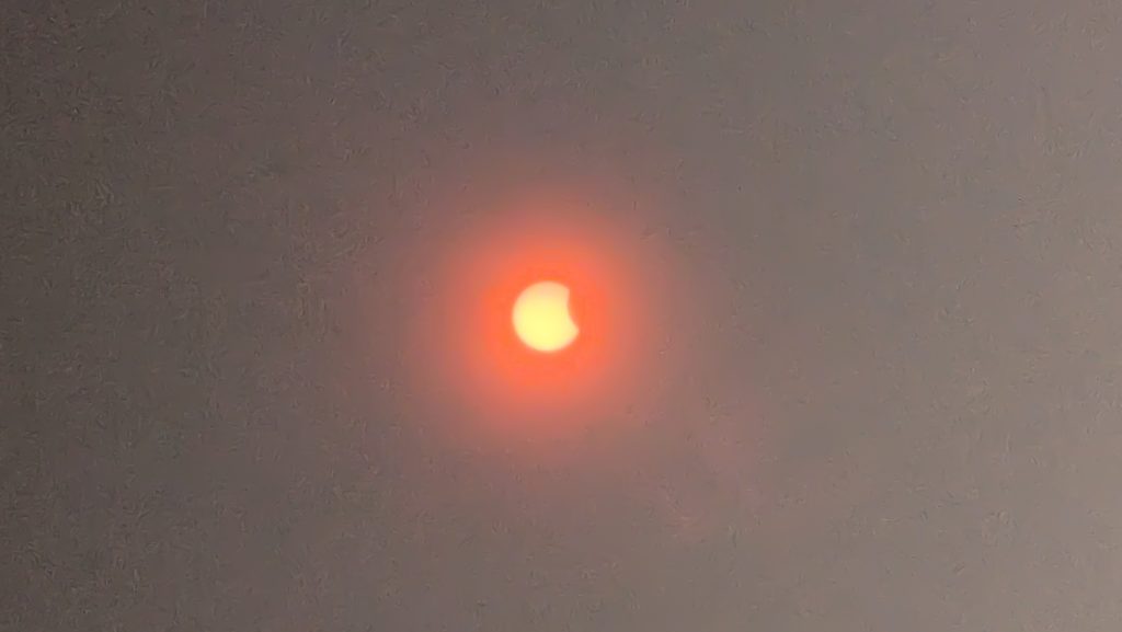 Éclipse solaire partielle rougeoyante dans un ciel brumeux.