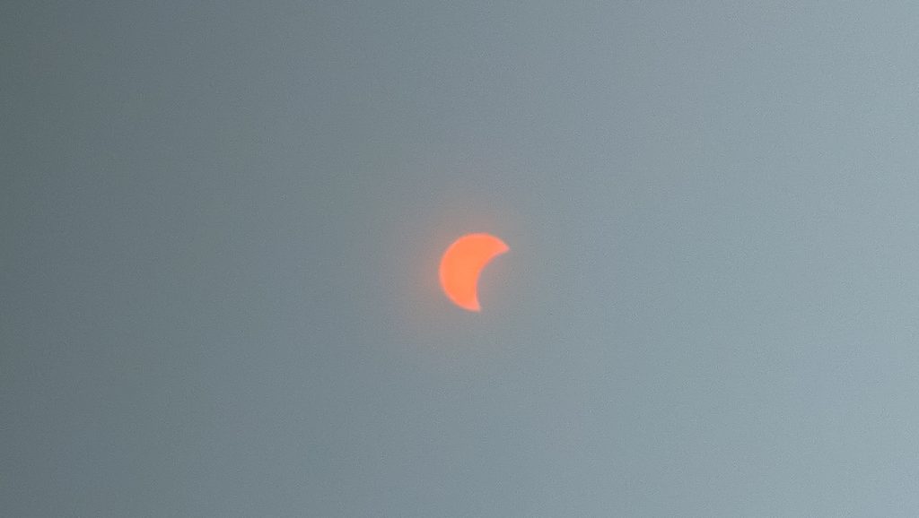 Éclipse solaire partielle orange dans un ciel gris et brumeux.