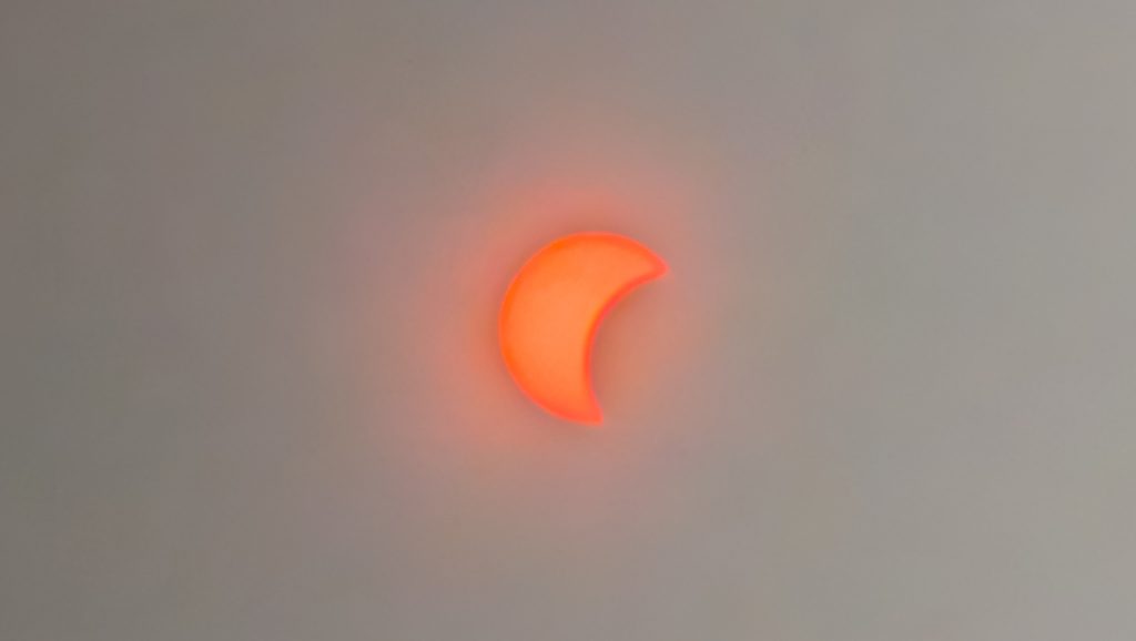 Éclipse solaire partielle orange vif sur fond gris.