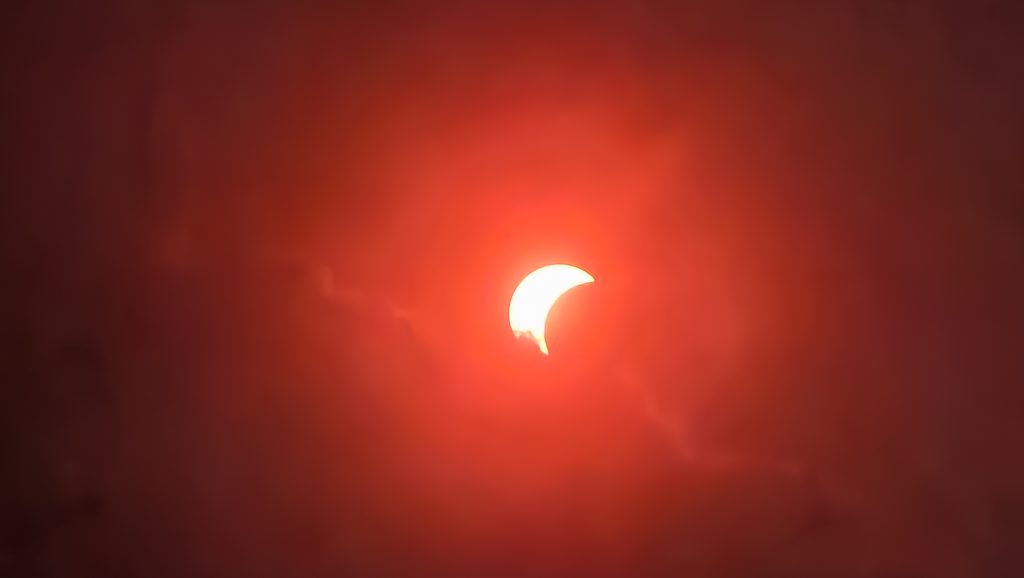 Éclipse solaire partielle apparaissant comme un croissant dans un ciel rouge orangé.