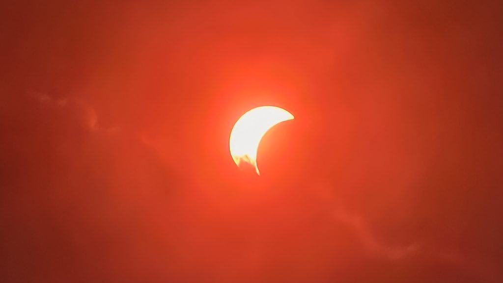 Éclipse solaire partielle contre un ciel rouge flamboyant et nuageux.