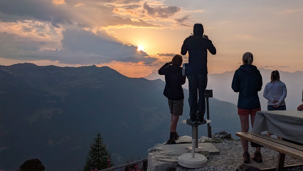 Personnes admirant un coucher de soleil spectaculaire sur les montagnes.