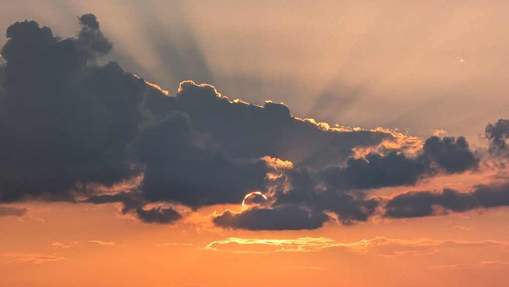 Coucher de soleil derrière des nuages sombres avec rayons lumineux.