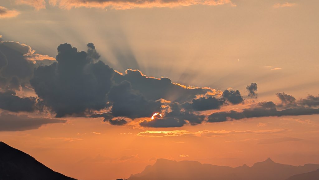 Coucher de soleil, nuages sombres, rayons de lumière, montagnes.