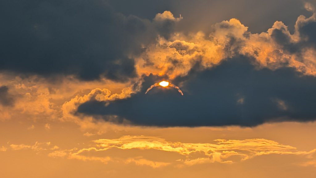 Soleil perçant nuages sombres, ciel orange et doré.