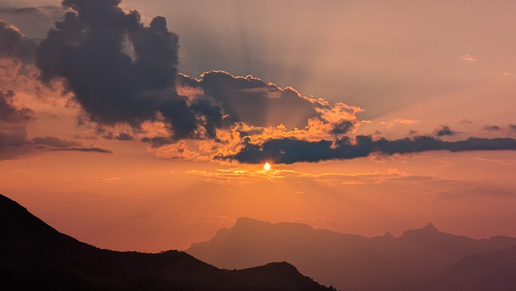 Coucher de soleil flamboyant sur les montagnes avec des nuages et rayons.