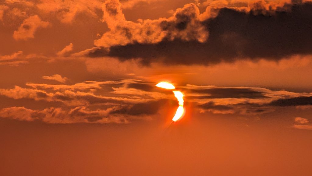 Coucher de soleil orange intense avec soleil fragmenté et nuages.