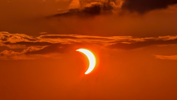 Éclipse solaire partielle orangée dans un ciel nuageux.