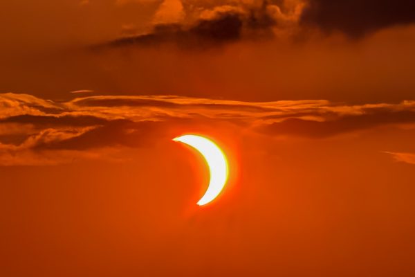 Éclipse solaire partielle orangée dans un ciel nuageux.