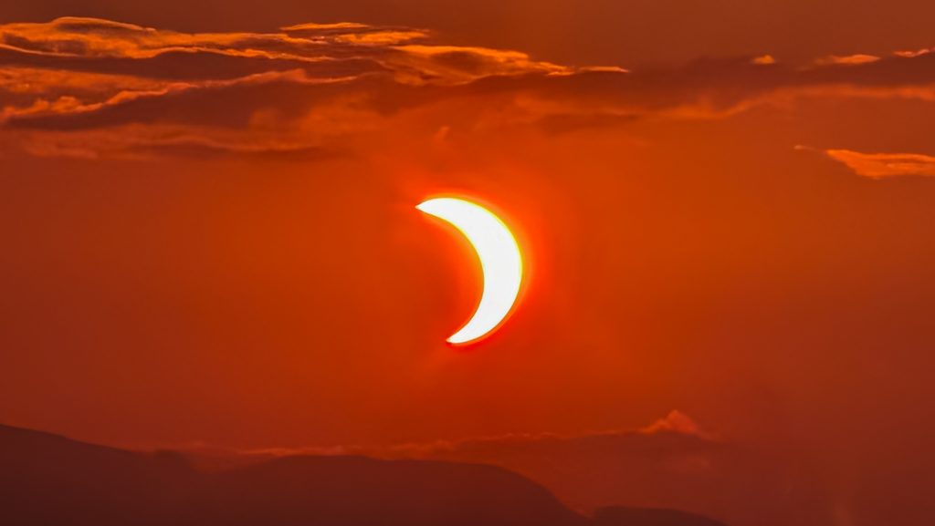 Éclipse solaire partielle, soleil en croissant sur ciel orange ardent.