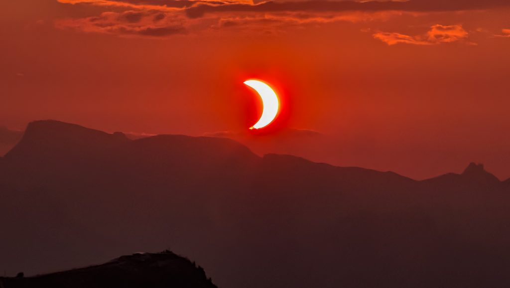 Éclipse solaire partielle au-dessus de montagnes sous un ciel rouge.