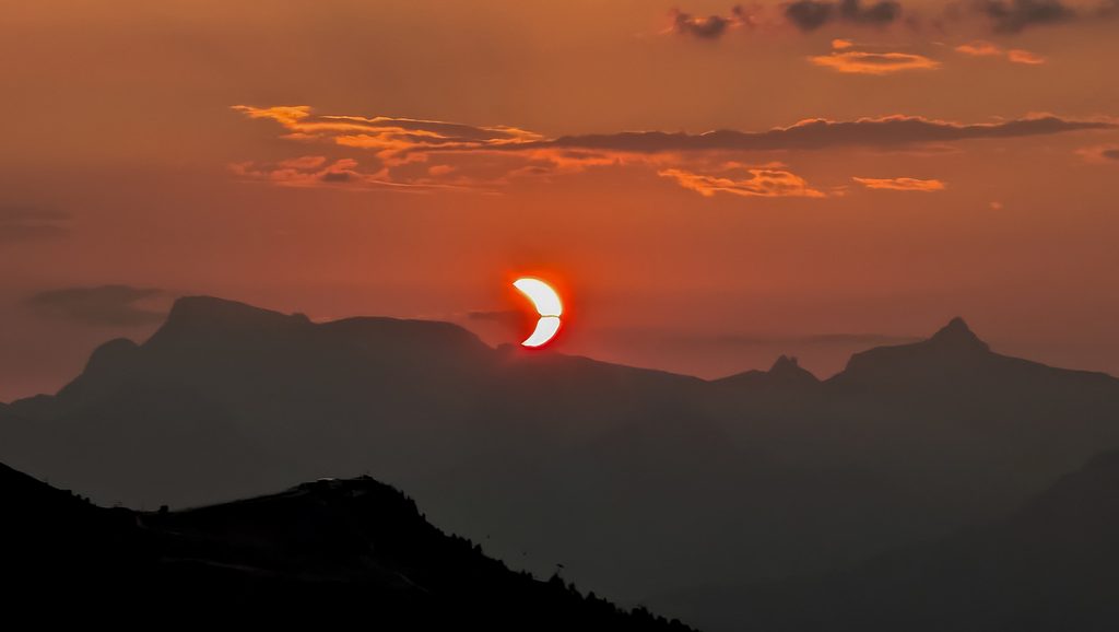Soleil en croissant rougeoyant sur silhouettes de montagnes au crépuscule.
