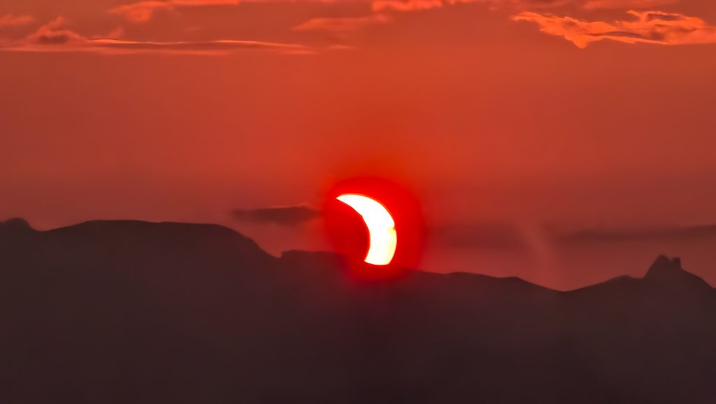 Éclipse solaire partielle au-dessus de montagnes au coucher du soleil.