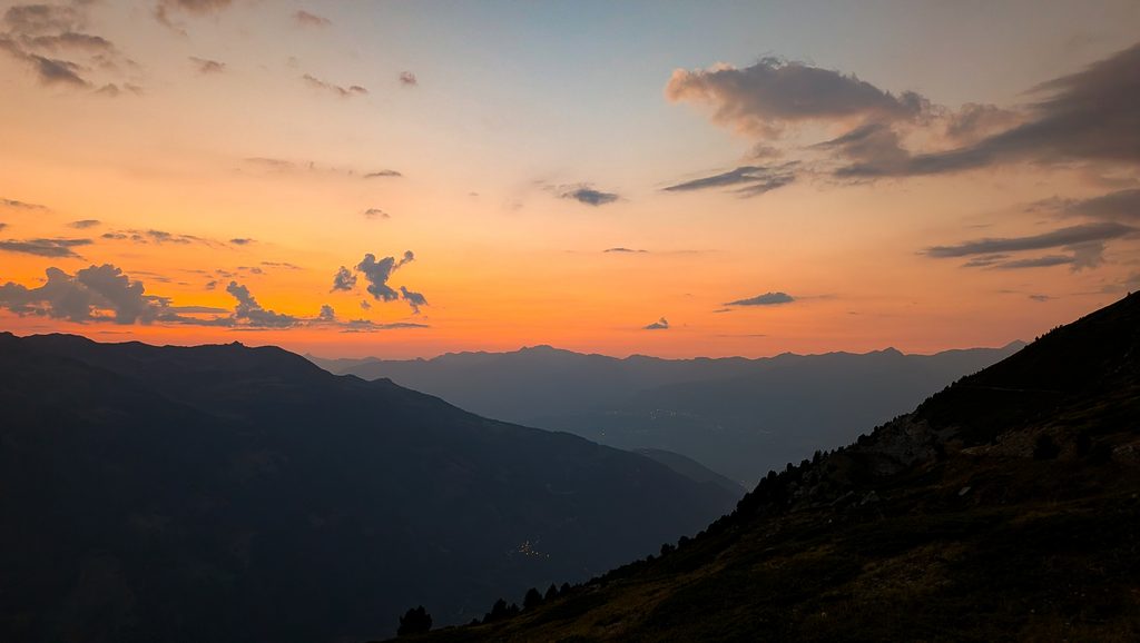 Coucher de soleil orange sur montagnes sombres avec nuages.