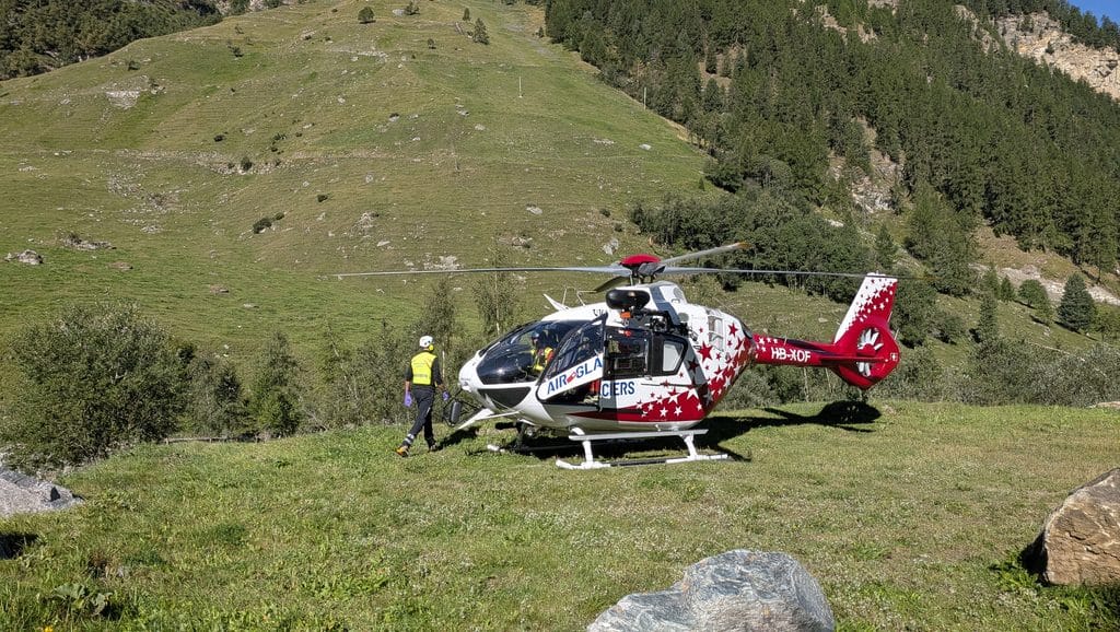 Hélicoptère de sauvetage Air Glaciers sur pente montagneuse herbeuse.
