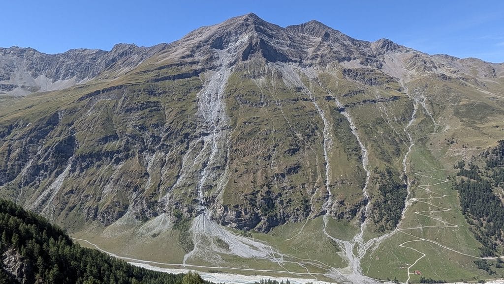 Vaste paysage montagneux rocheux avec route sinueuse et vallée verte.