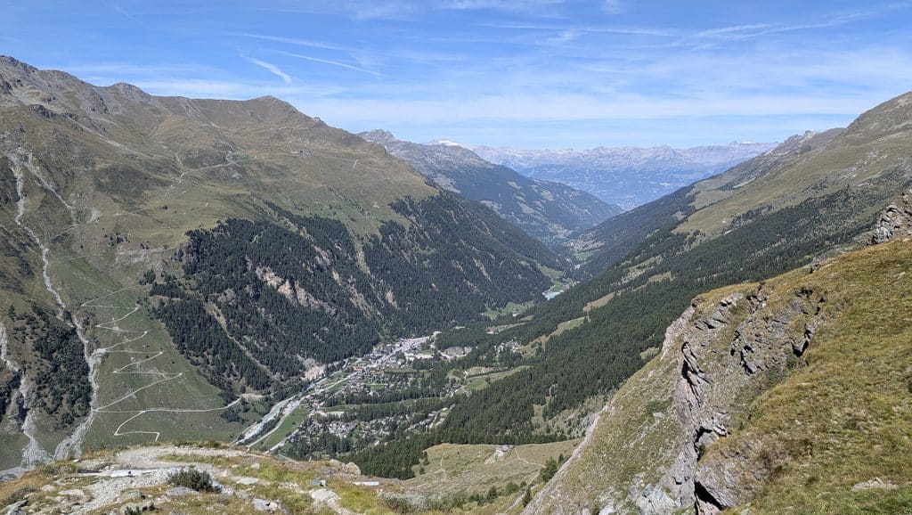 Vue aérienne d'une vallée alpine avec village et montagnes boisées.